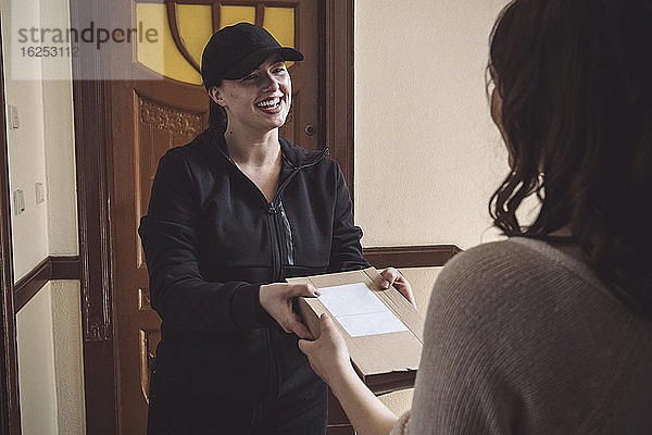 Lächelnde Zustellerin  die dem Kunden ein Paket an der Haustür ausliefert
