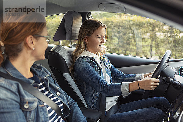 Mutter unterrichtet lächelndes Teenager-Mädchen beim Autofahren am Wochenende