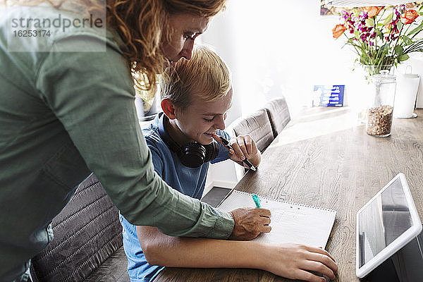 Mutter hilft lächelndem Sohn beim Lernen zu Hause