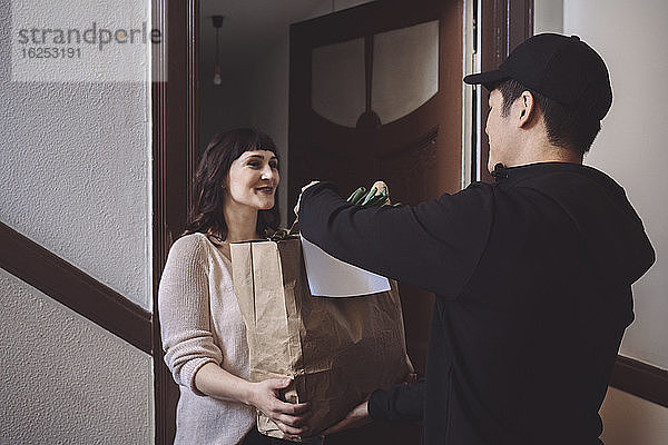 Lächelnder Kunde spricht mit dem Lieferanten  während er eine Gemüsetüte vor die Tür hält