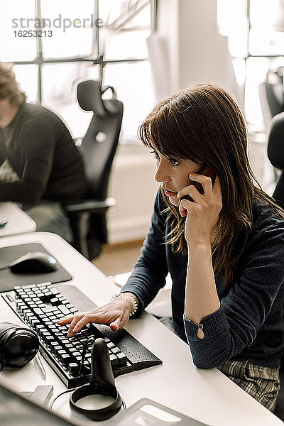 Unternehmerin  die während eines Telefongesprächs am Arbeitsplatz an der Programmierung arbeitet