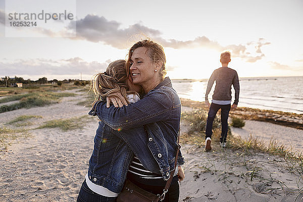 Lächelnde Mutter umarmt Tochter am Wochenende am Strand