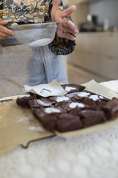 Frau bestreut gebackene Brownies in der Küche mit Puderzuckerherzen