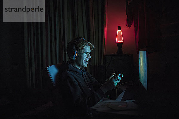 Lächelnder Teenager spielt Videospiel am Computer im dunklen Schlafzimmer