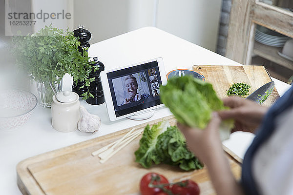 Frau beim Kochen und Video-Chat mit Freunden auf digitalem Tablet-Bildschirm