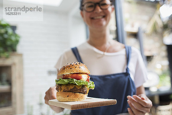 Porträt einer lächelnden Frau mit Cheeseburger auf Schneidebrett