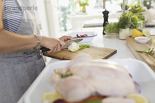 Frau schneidet Kräuter für Hühnergericht in der Küche