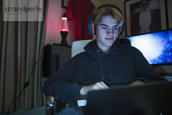 Teenager-Junge mit Headset mit Laptop im dunklen Schlafzimmer