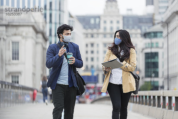 Geschäftsleute mit Gesichtsmasken im Gespräch auf einer städtischen Fußgängerbrücke