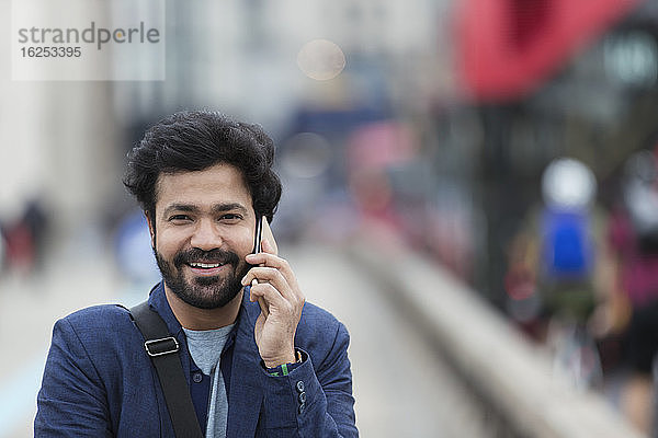 Porträt eines lächelnden Geschäftsmannes  der im Freien mit einem Smartphone telefoniert