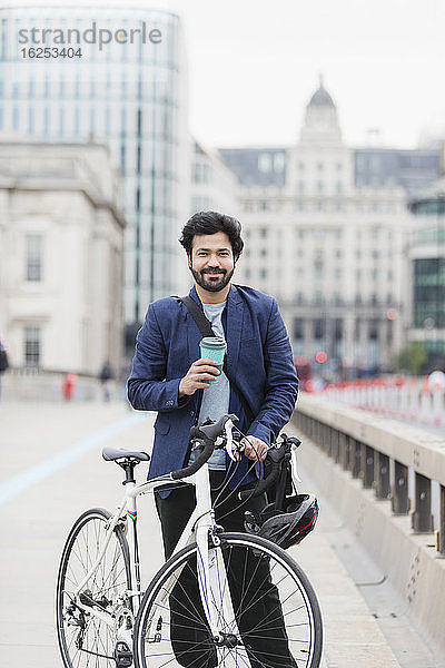 Porträt eines lächelnden Geschäftsmannes mit Kaffee und Fahrrad auf der Stadtbrücke