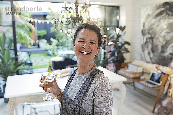 Porträt einer glücklichen Frau  die in der Küche Weißwein trinkt