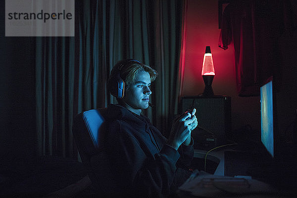 Teenager-Junge mit Headset spielt Videospiel in dunklem Schlafzimmer