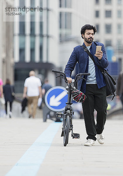 Geschäftsmann mit Smartphone geht Fahrrad auf Stadtbrücke