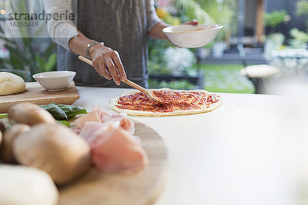 Frau streicht Tomatensauce auf Pizzateig