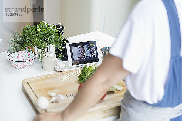 Frau beim Kochen und Video-Chat mit Freunden auf digitalem Tablet-Bildschirm