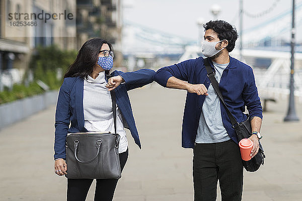 Geschäftsleute mit Gesichtsmasken berühren auf der Straße in der Stadt die Ellbogen