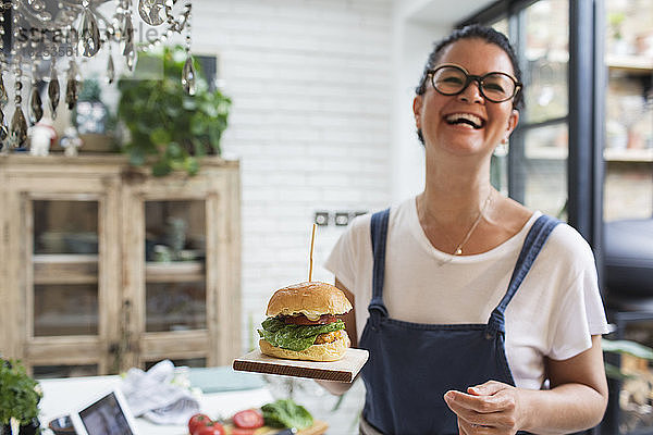 Porträt lachende Frau mit Cheeseburger auf Schneidebrett