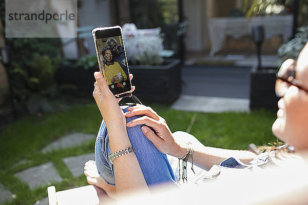 Frau auf sonniger Terrasse im Video-Chat mit Freunden auf dem Bildschirm eines Smartphones