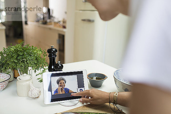 Frau im Video-Chat mit Freunden auf digitalem Tablet-Bildschirm in der Küche