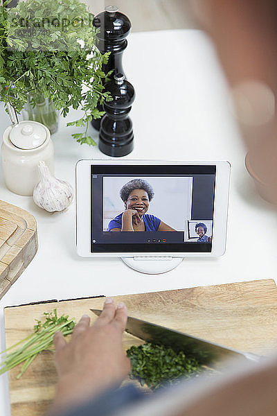 Frau beim Kochen und Video-Chat mit Freunden auf digitalem Tablet-Bildschirm