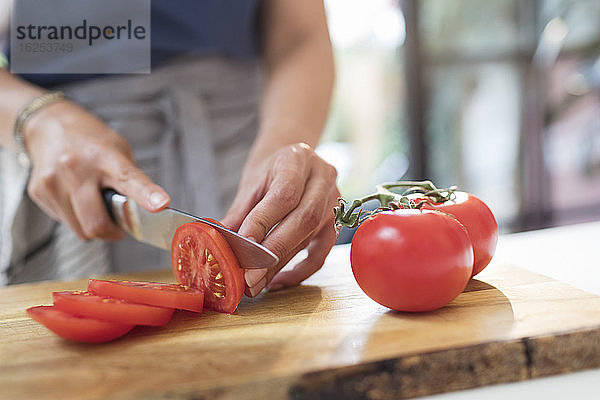 Nahaufnahme einer Frau mit Messer  die rote Tomaten auf einem Schneidebrett in Scheiben schneidet