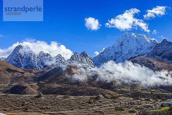 Touristen wandern auf dem Gokyo-Trekkingpfad durch die herbstlich gefärbte Tundra  mit weißen  schneebedeckten Himalaya-Gipfeln  die sich im Hintergrund erheben  vorbei an Teehäusern und Sherpa-Häusern  Solokhumbu-Distrikt  Sagarmatha-Nationalpark; Nepal