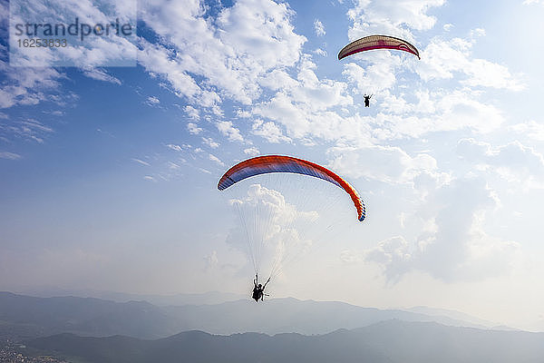 Gleitschirmflieger fliegen hoch über der Stadt Pokhara  Nepal im Himalaya-Gebirge  an einem sonnigen  verrauchten Tag; Pokhara  Gandaki Pradesh  Nepal