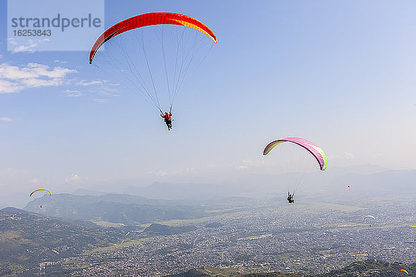 Gleitschirmflieger fliegen hoch über der Stadt Pokhara  Nepal im Himalaya-Gebirge  an einem sonnigen  verrauchten Tag; Pokhara  Gandaki Pradesh  Nepal