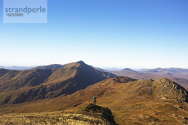 Einzelner männlicher Wanderer  der an einem sonnigen Tag auf einem Hügel steht und auf die Berge von Kerry in der Ferne schaut; Grafschaft Kerry  Irland