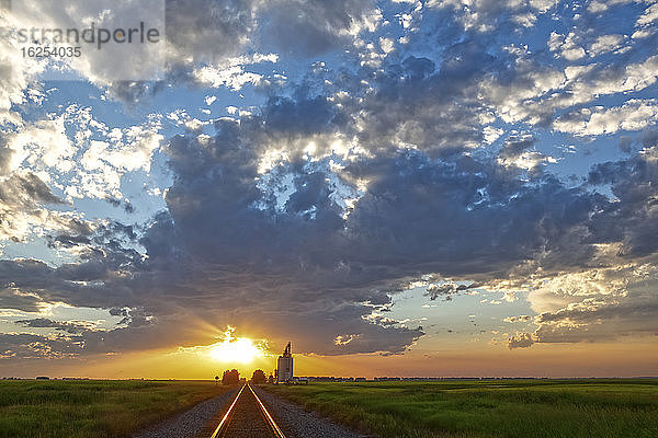 Ein Getreidelager bei Sonnenuntergang mit heller Sonne über dem Horizont; Alberta  Kanada