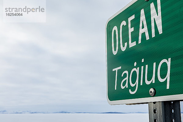 Straßenschild 'Ocean Tagiuq' im Winter  auf Englisch und Inupiaq  gegenüber dem Kotzebue-Sund im Winter; Kotzebue  Alaska  Vereinigte Staaten von Amerika