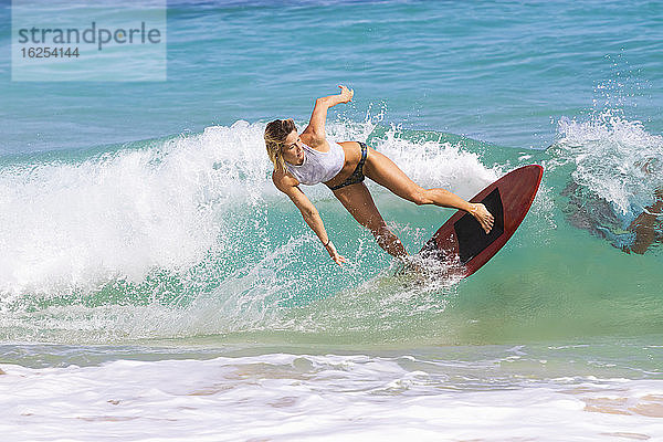 Eine junge Frau  die auf einer Welle vor Sandy Beach  Oahu; Oahu  Hawaii  Vereinigte Staaten von Amerika  auf dem Skimboard fährt