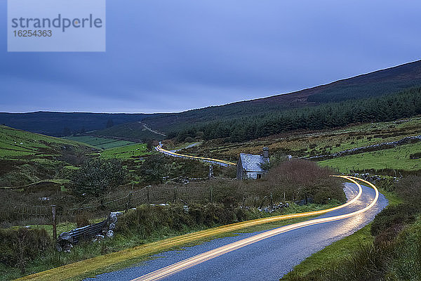 Autolichter auf einer kurvenreichen Straße in den Kockmealdown Mountains an einem bedeckten  bewölkten Abend; Grafschaft Tipperary  Irland