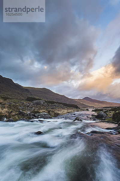 Wildwasserfluss stürzt bei Sonnenuntergang mit dramatischem Himmel durch das Schwarze Tal im Herzen der Kerry-Berge; Grafschaft Kerry  Irland