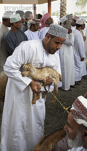 Traditionell gekleidete omanische Männer inspizieren Ziegen auf dem Ziegenmarkt im Friday Souk