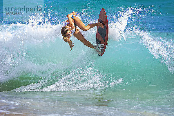 Eine junge Frau reitet auf einem Skimboard auf einer Welle vor Sandy Beach  Oahu; Oahu  Hawaii  Vereinigte Staaten von Amerika