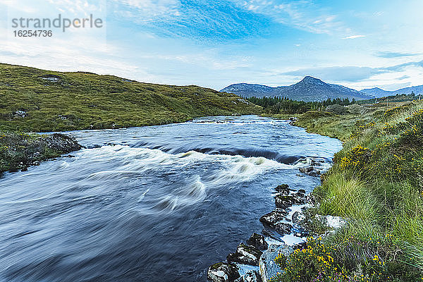 Kleine Stromschnellen auf einem durch Connemara fliessenden Fluss mit einem Berg im Hintergrund an einem Tag mit blauem Himmel; Connemara  County Galway  Irland