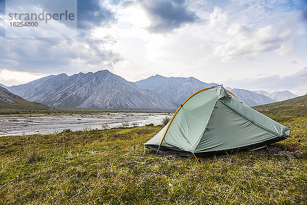 Grün-graues Rucksackzelt  das im Sommer in der Tundra aufgestellt wird  an einem Sommertag in den Brooks Range-Bergen  Arctic National Wildlife Refuge  mit dem Marsh Fork River im Hintergrund; Alaska  Vereinigte Staaten von Amerika