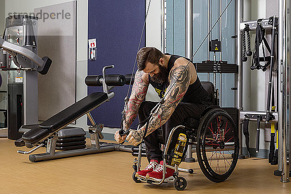 Ein querschnittsgelähmter Mann trainiert in einer Fitnesseinrichtung mit einem Crossover-Gewichtsscheibenhebegerät; Sherwood Park  Alberta  Kanada