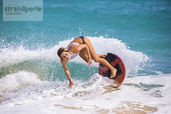 Eine junge Frau  die auf einer Welle vor Sandy Beach  Oahu; Oahu  Hawaii  Vereinigte Staaten von Amerika  auf dem Skimboard fährt