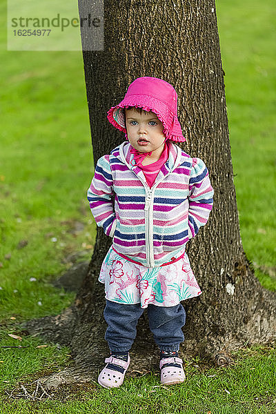 Porträt eines jungen Mädchens in farbenfroher Kleidung  das im Park vor einem Baum steht; Surrey  British Columbia  Kanada