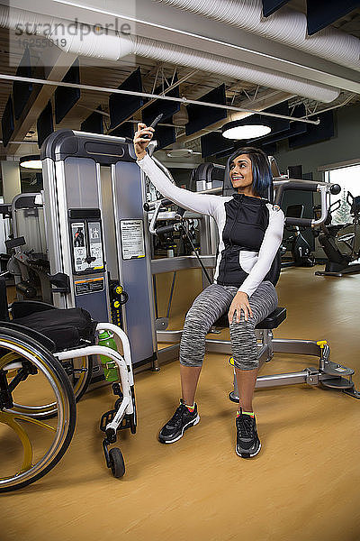 Eine querschnittsgelähmte Frau  die sich nach dem Training mit einer Überkopfpresse in einer Fitnesseinrichtung ausruht und ein Selbstporträt aufnimmt; Sherwood Park  Alberta  Kanada