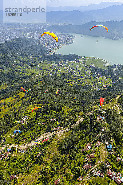 Luftaufnahme einer Gruppe von Gleitschirmfliegern  die über Sarangkot fliegen und in der Thermik spielen  mit der Stadt Pokhara und dem Phewa-See in der Ferne  an einem bewölkten Herbsttag; Pokhara  Nepal