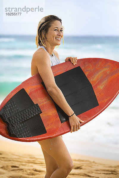 Eine junge Frau steht am Sandstrand von Oahu mit einem Skimboard; Oahu  Hawaii  Vereinigte Staaten von Amerika