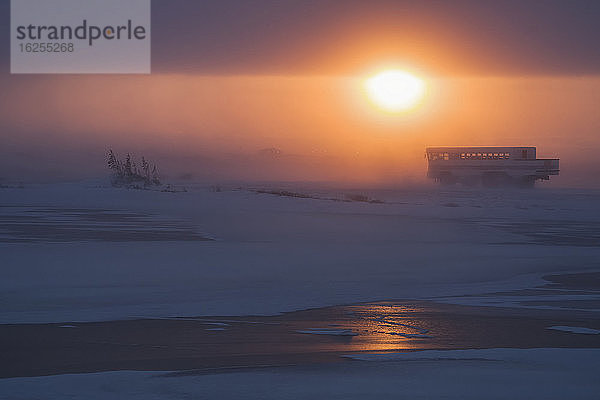 Sonnenuntergang beleuchtet den wehenden Schnee  während sich ein Tour-Buggy entlang der Küste der Hudson Bay auf den Heimweg macht; Churchill  Manitoba  Kanada