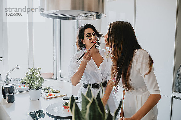 Zwei Frauen mit braunem Haar stehen in einer Küche und essen Sushi.