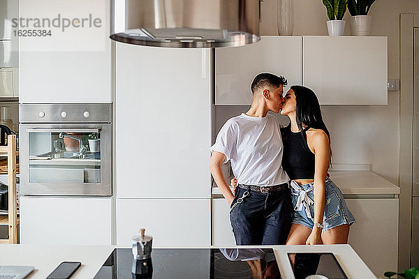 Junges lesbisches Paar steht in der Küche und küsst sich.