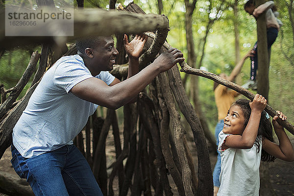 Vater und Tochter bauen ein Tipi mit Zweigen im Wald