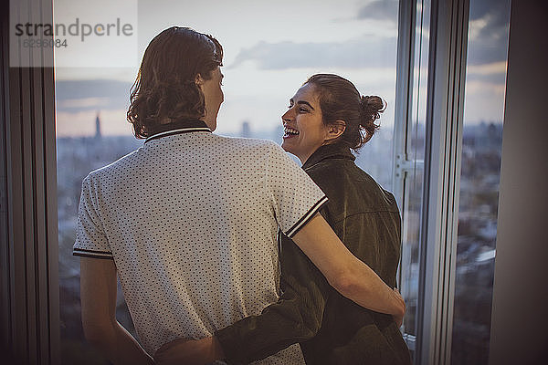Glückliches junges Paar umarmt sich am Hochhausfenster